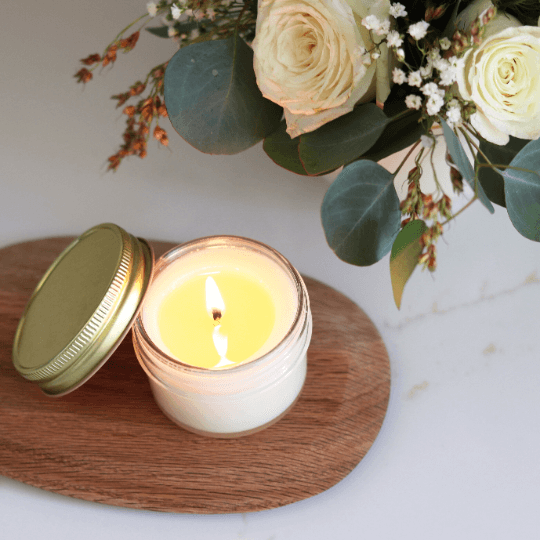 Eco-friendly baptism candle favor with wildflower label next to a floral arrangement, perfect for special celebrations.