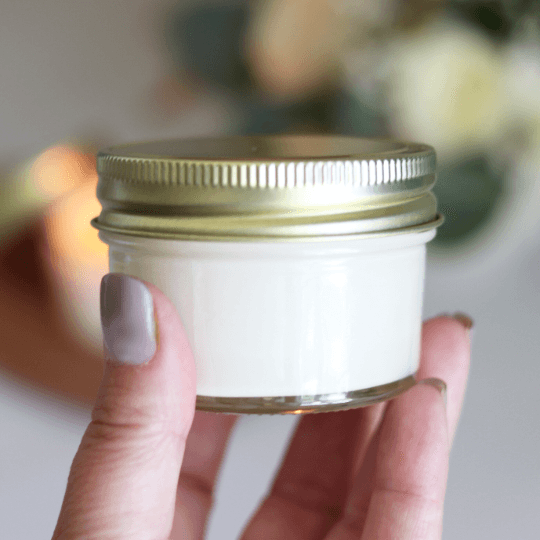 Person holding a small glass jar of eco-friendly baptism candle favor with a gold lid.